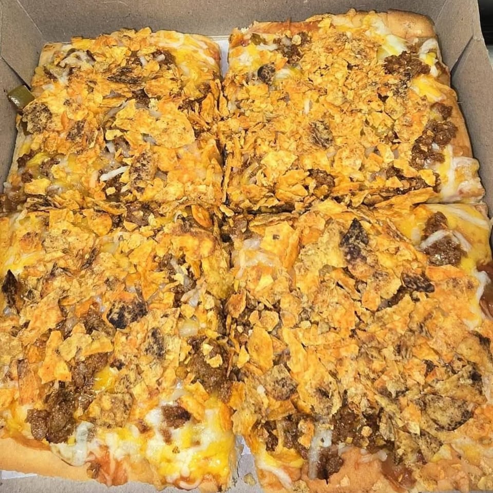 Buzzi's Pizza taco pizza, topped with crushed chips and ground beef, in a cardboard box.