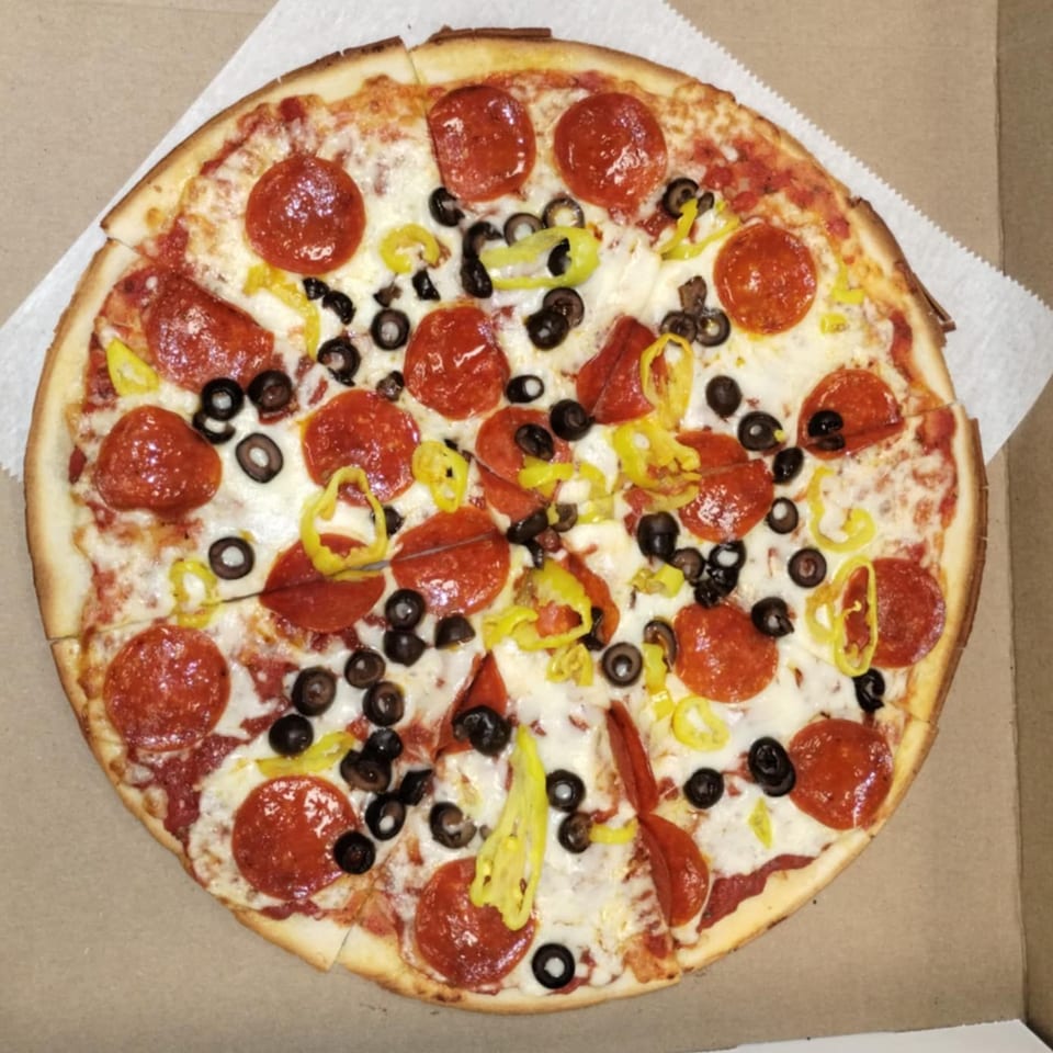 A whole Buzzi's Pizza with pepperoni, black olives, and banana peppers in a cardboard box.
