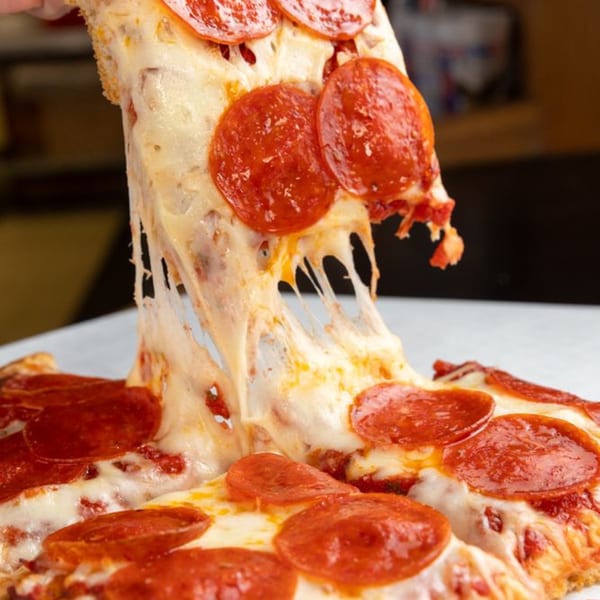 A slice of Buzzi's pepperoni pizza being lifted, with melted cheese stretching from the pie.