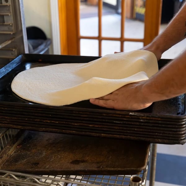 Hands stretching fresh pizza dough onto a dark baking pan at Buzzi's Pizza.