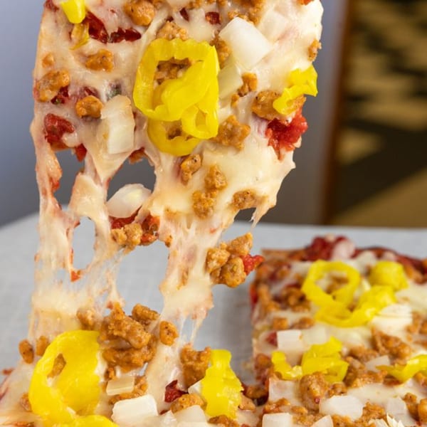 A slice of Buzzi's Pizza with sausage, onions, and banana peppers, lifted with melted cheese stretching.