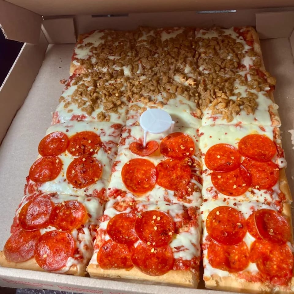 A Buzzi's Pizza box holds a rectangular pizza with half sausage and half pepperoni toppings.