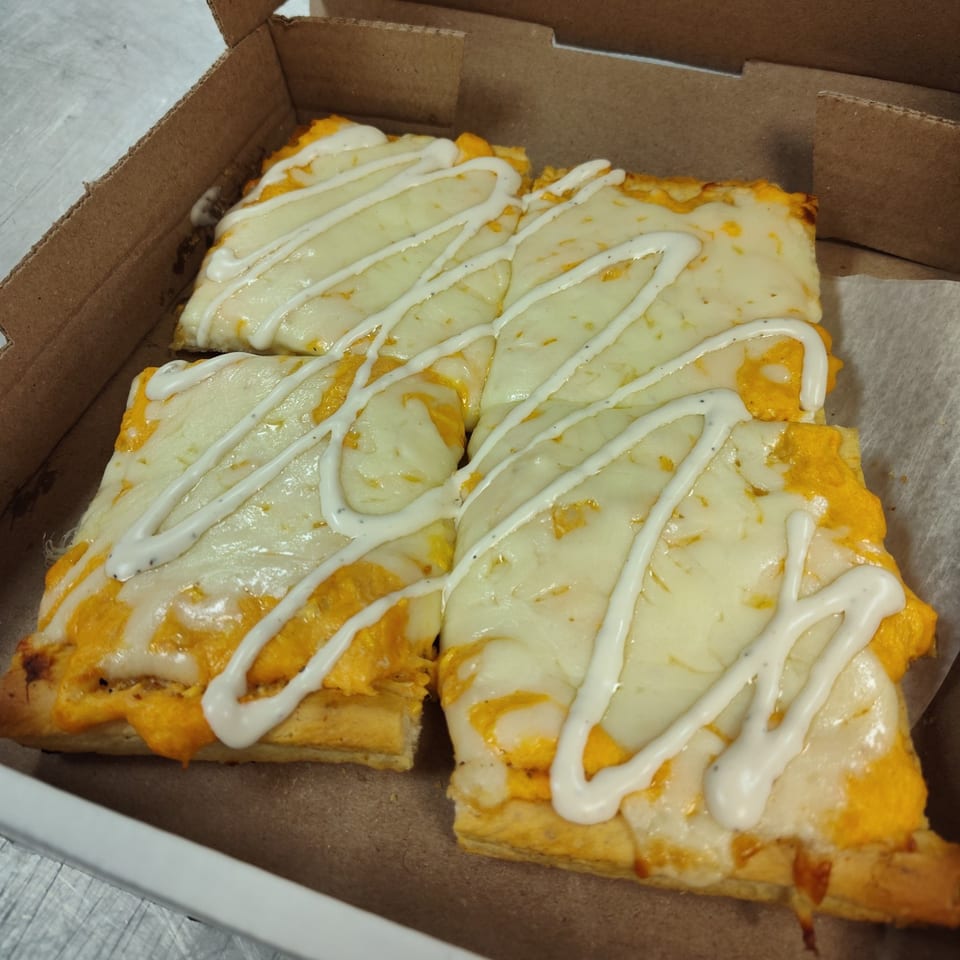 Four rectangular slices of Buzzi's Pizza with melted cheese and a white sauce drizzle in a box.